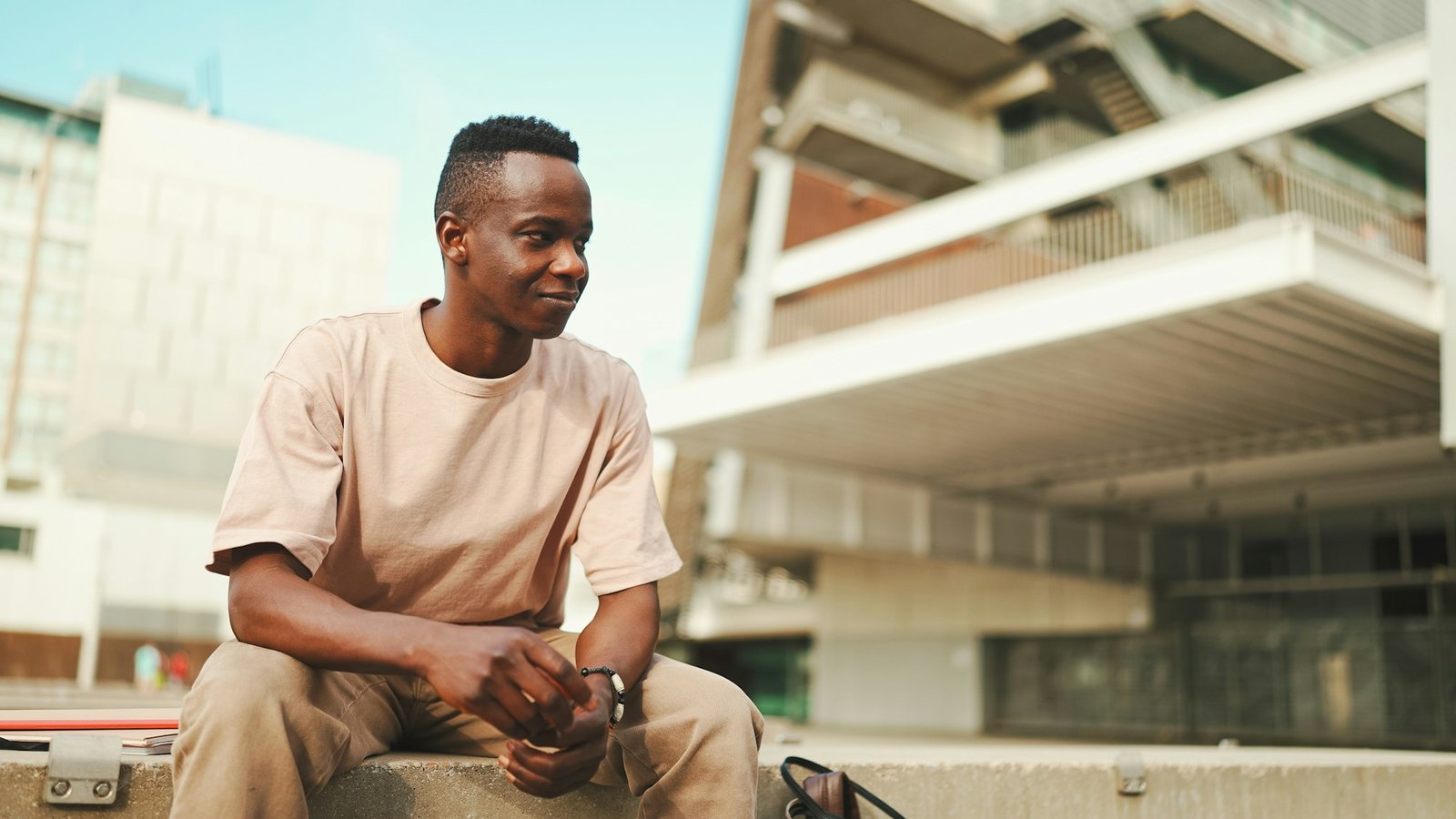 Smiling young african student sitting outside of university, looking around